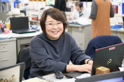 横山理恵さんが職場のPCの前で微笑んでいる様子